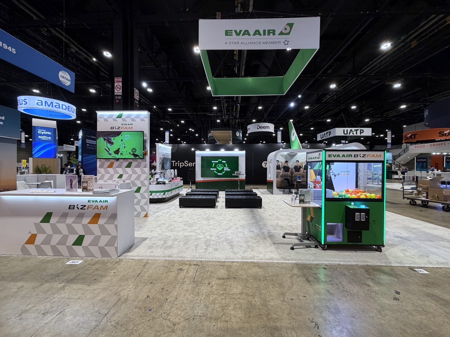 EVA Air booth with a hanging sign above a BIZFAM counter, a green gacha machine, and a tail-fin cutout
