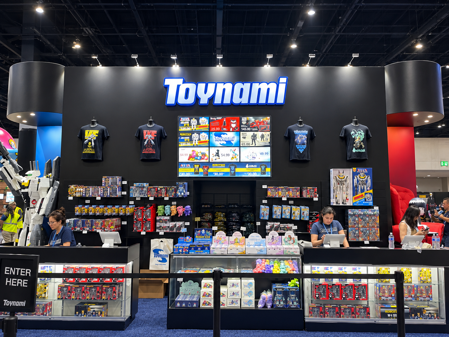 Toynami booth wall with the Toynami wordmark, shirts on display, and glass counters of boxed collectibles