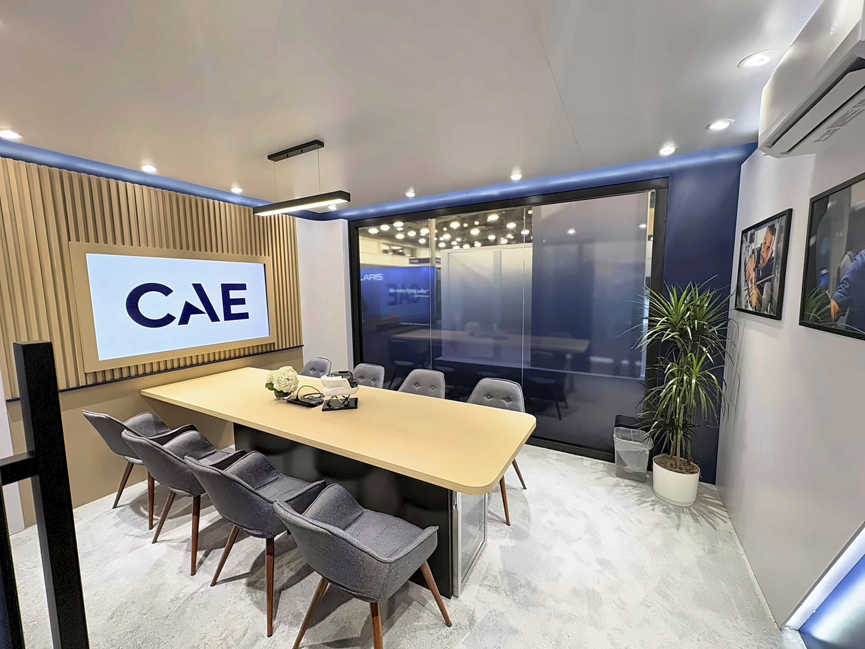 Meeting room with a slatted wood wall, a screen showing the CAE logo, a long table, and six grey chairs