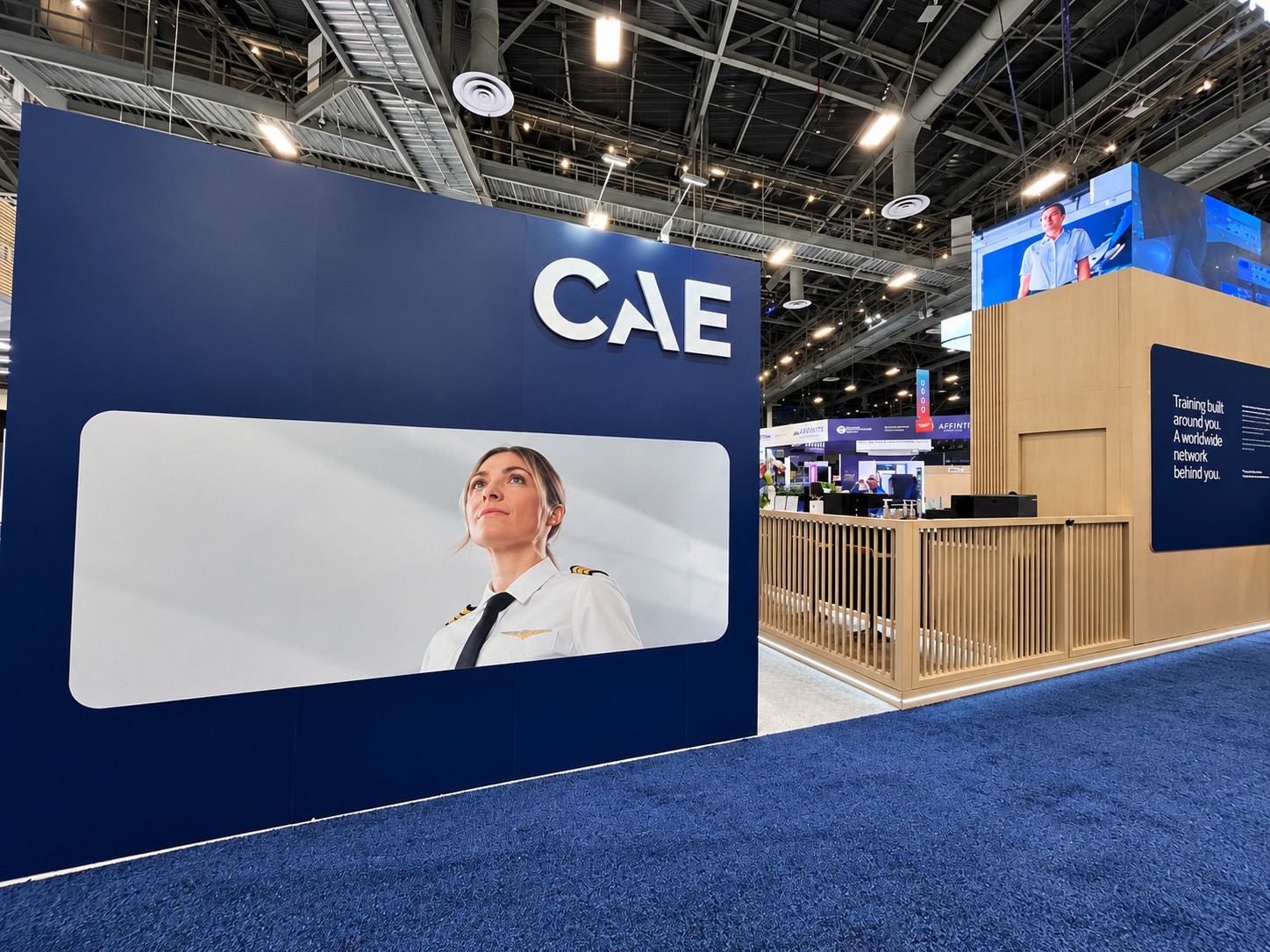 Navy wall with a lightbox portrait of a pilot in uniform beside white CAE letters.