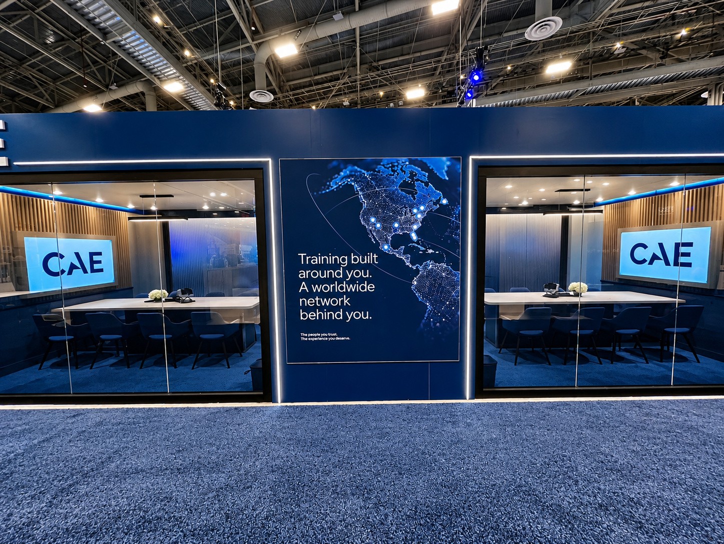Two glass meeting rooms flanking a navy panel with a glowing map and the CAE logo on each screen.