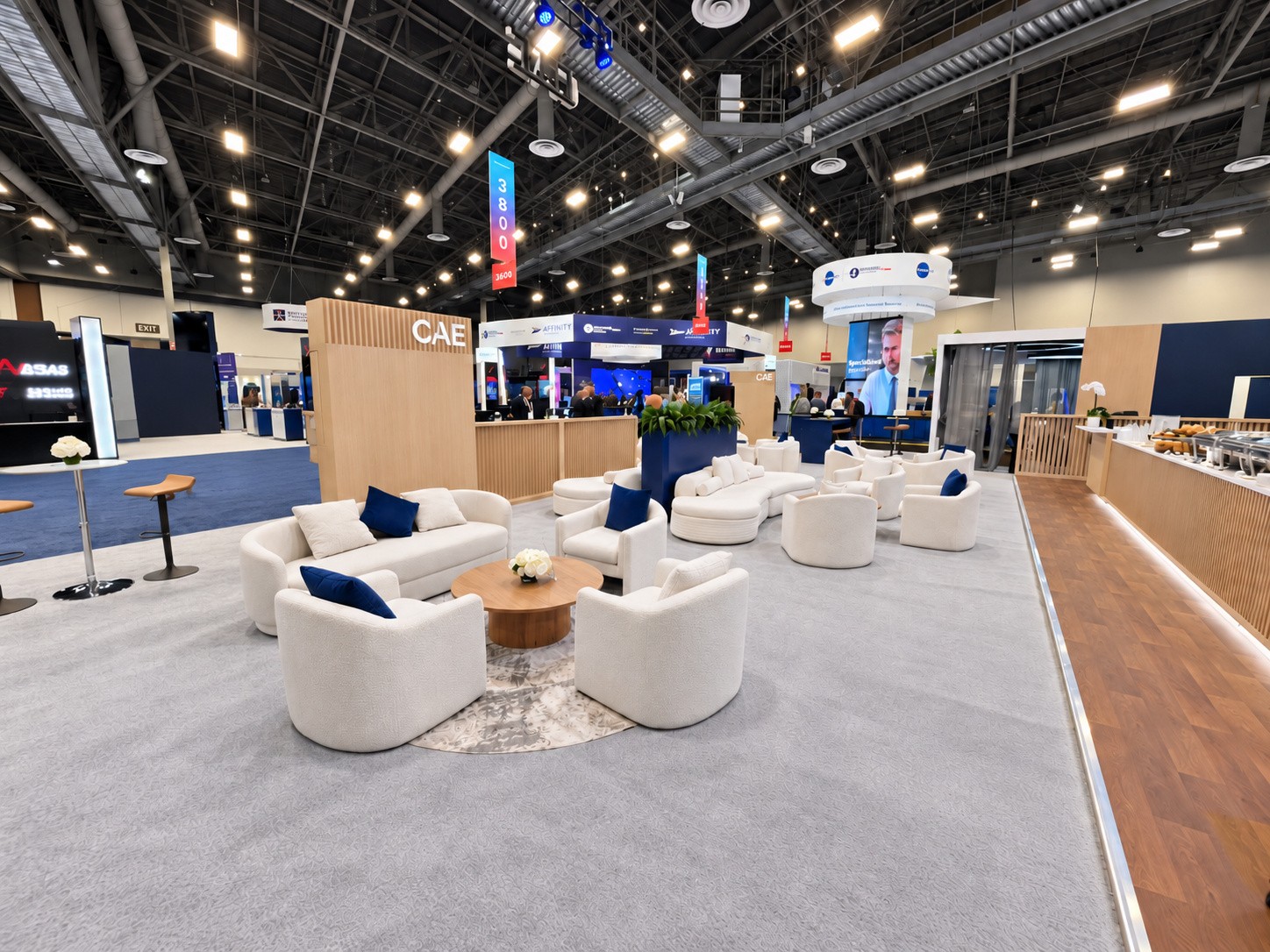 Wide view of the CAE island with lounge seating, wood slat walls, and white CAE letters.