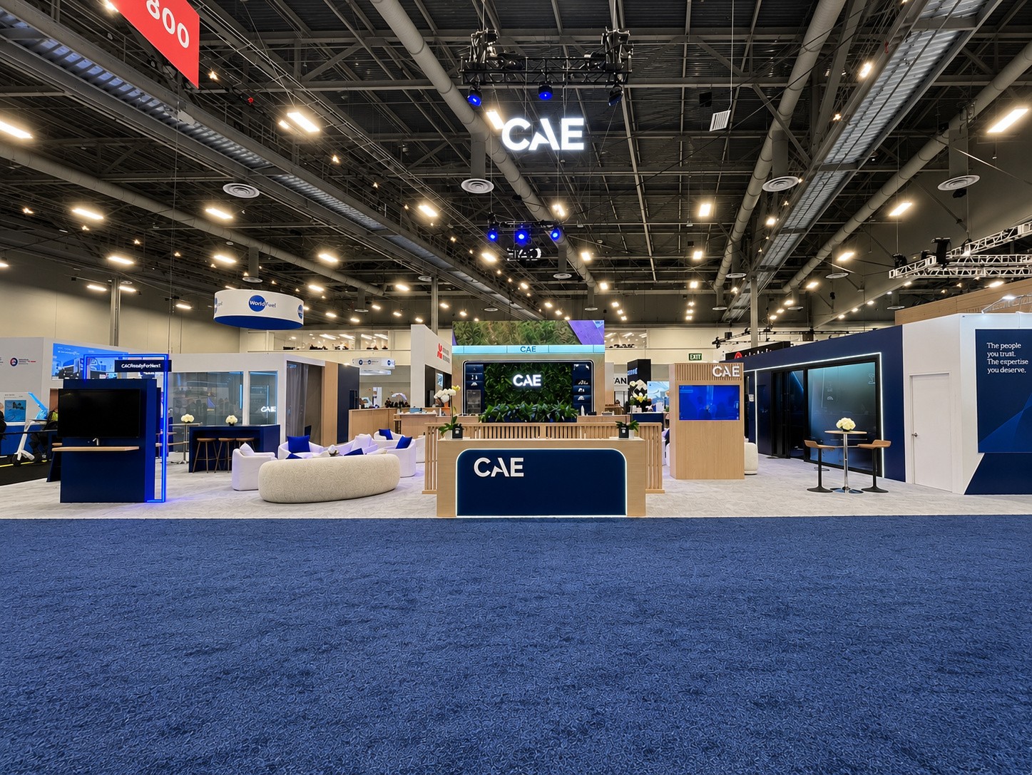 wide view of the CAE island from the aisle with a hanging CAE sign, lounge seating, and the café counter.