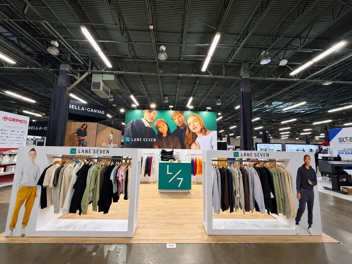 Lane Seven island with two white garment racks, a green L/7 counter, and a teal wall with four models