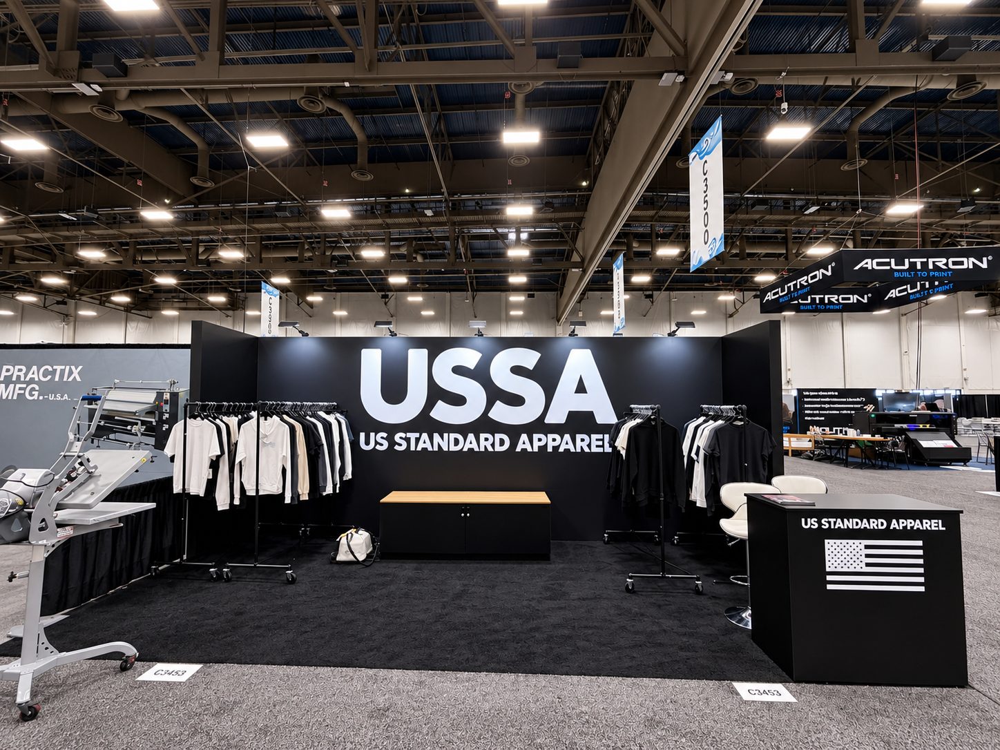 US Standard Apparel booth front with the USSA wall, racks of mixed garments, and the black podium